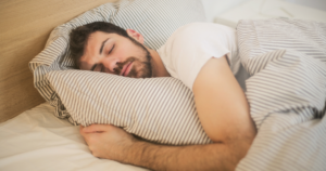 Man sleeping in bed, hugging a striped pillow under striped bedding.