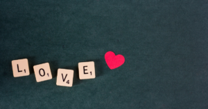 Scrabble tiles spell 'LOVE' with a red heart on a dark teal background.