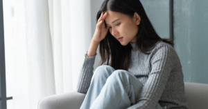 Woman sitting on a sofa, hand on her forehead, looking down in distress.