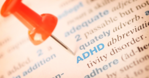 Close-up of a red pushpin pinning a page with the word ADHD highlighted in blue on the text.