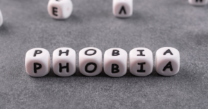 White letter dice spelling'PHOBIA' on a gray textured surface, forming the word.