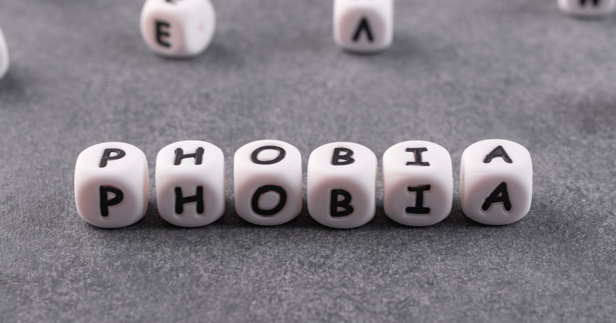 - Shine Mental Health White letter dice spelling 'PHOBIA' on a gray textured surface, forming the word.