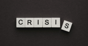 White letter tiles spell'CRISIS' on a dark background with an extra, tilted 'S' tile off to the right.