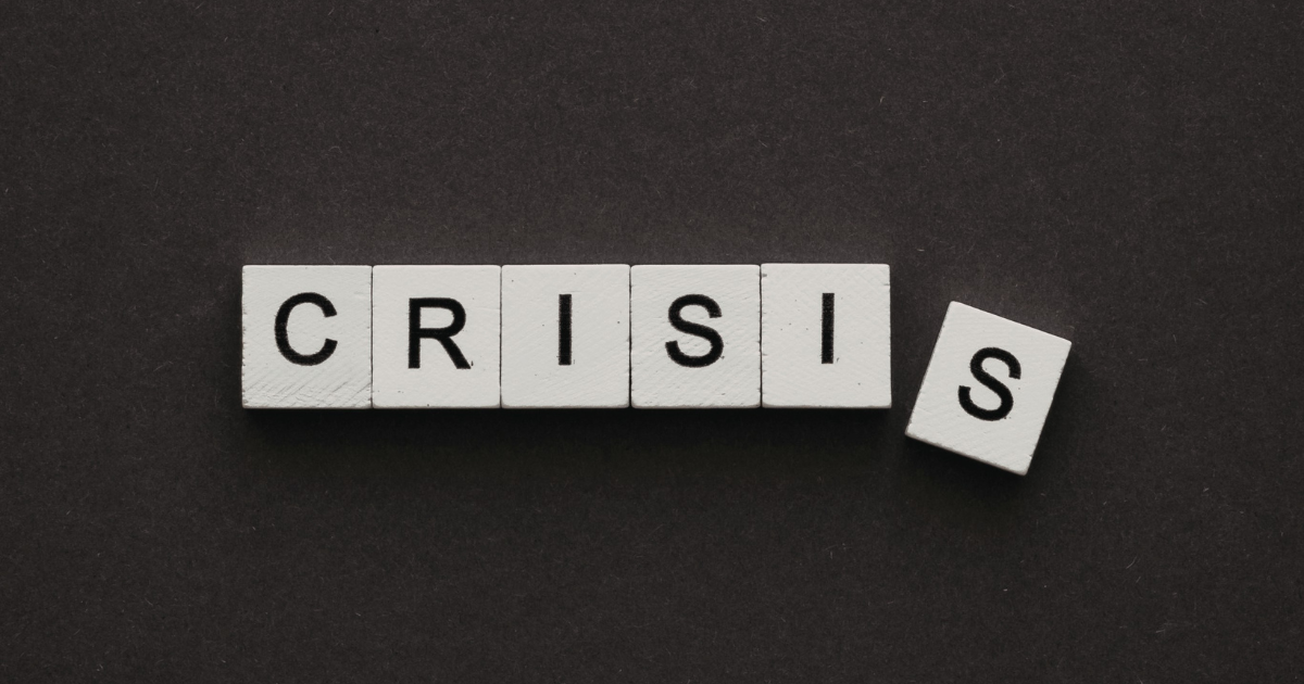 White letter tiles spell 'CRISIS' on a dark background with an extra, tilted 'S' tile off to the right.