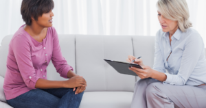 Counselor taking notes on a clipboard while client talks during a therapy session.