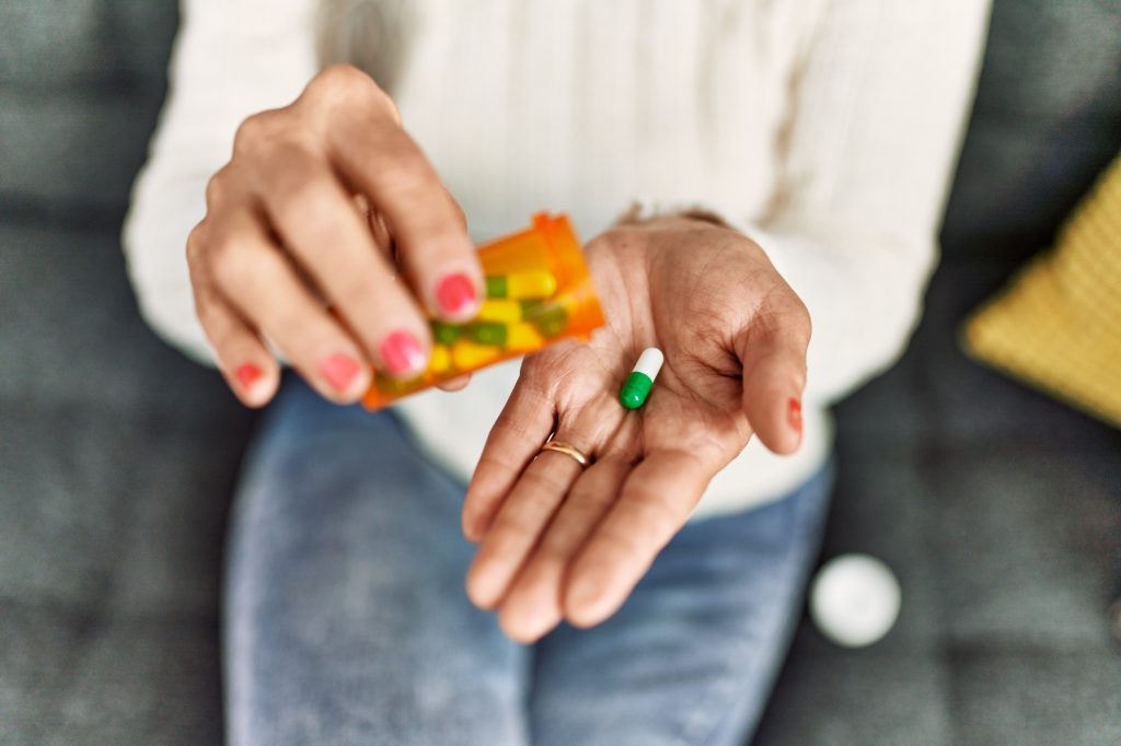 Person pours a green capsule from an orange pill bottle into their cupped hand on a couch surface