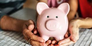 Pink piggy bank cradled in elderly hands on a checkered table, symbolizing saving for retirement.