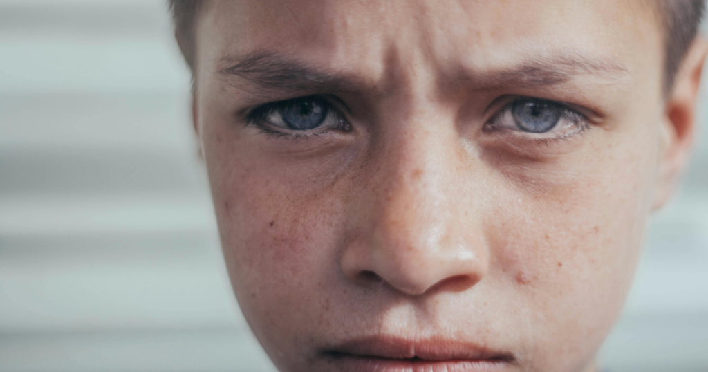 adhd-paralysis-breaking-free-guide-image-1 - Shine Mental Health Close-up of a young boy's face with a furrowed brow and blue eyes, looking intently ahead.