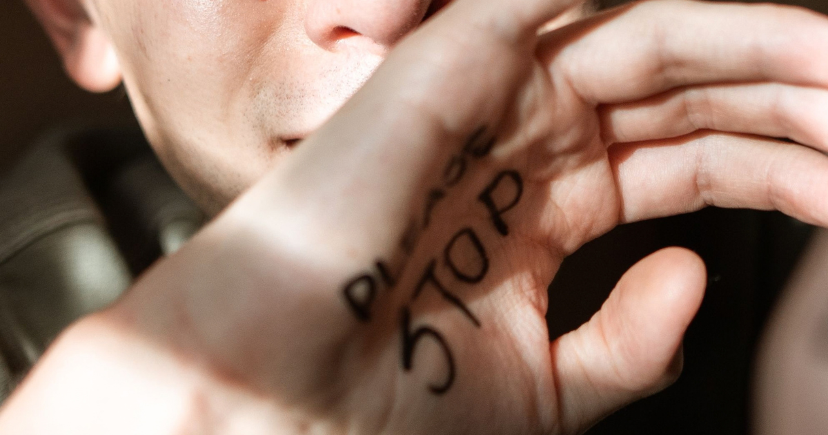 Close-up of a person's hand with the word STOP written on the palm; face partially visible in the background.