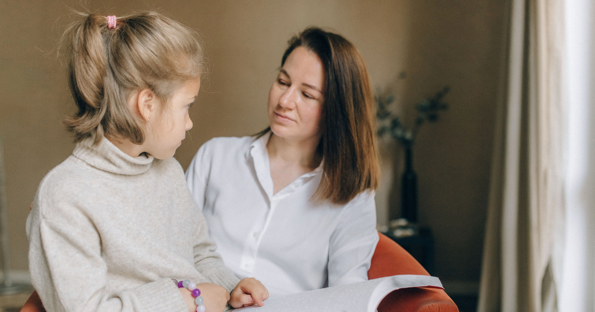 Mother and daughter sit together in a cozy room, looking at a notebook as they read.